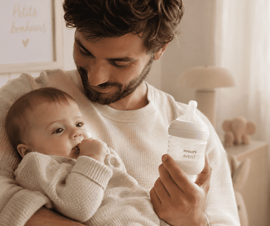 père avec son bébé  dans les bras qui tient un biberon de la marque philips avent natural